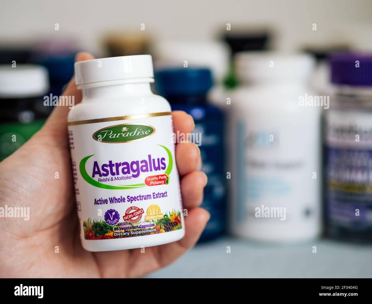 Moscow, Russia - March 09, 2021: Jar with Astragalus capsules in female hand and others nutrition supplements in blurred background. White plastic jar Astragalus by Paradise Herbs for immune support Stock Photo