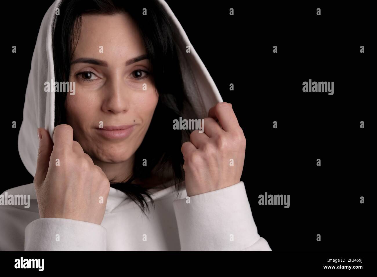 Portrait of beautiful mature brunette woman dressed in white hoodie isolated on black backdrop, copy space Stock Photo