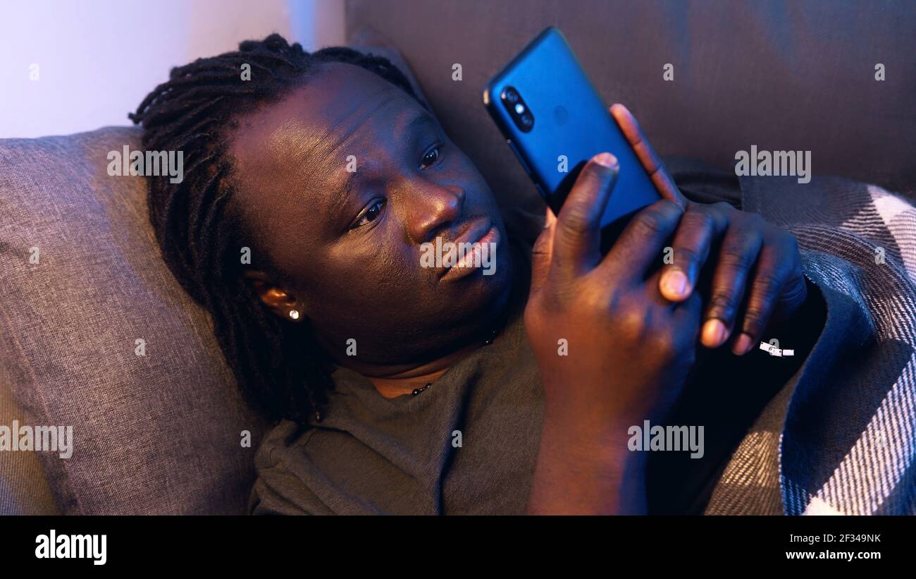 Bored black man using smartphone while resting on the couch. High quality photo Stock Photo