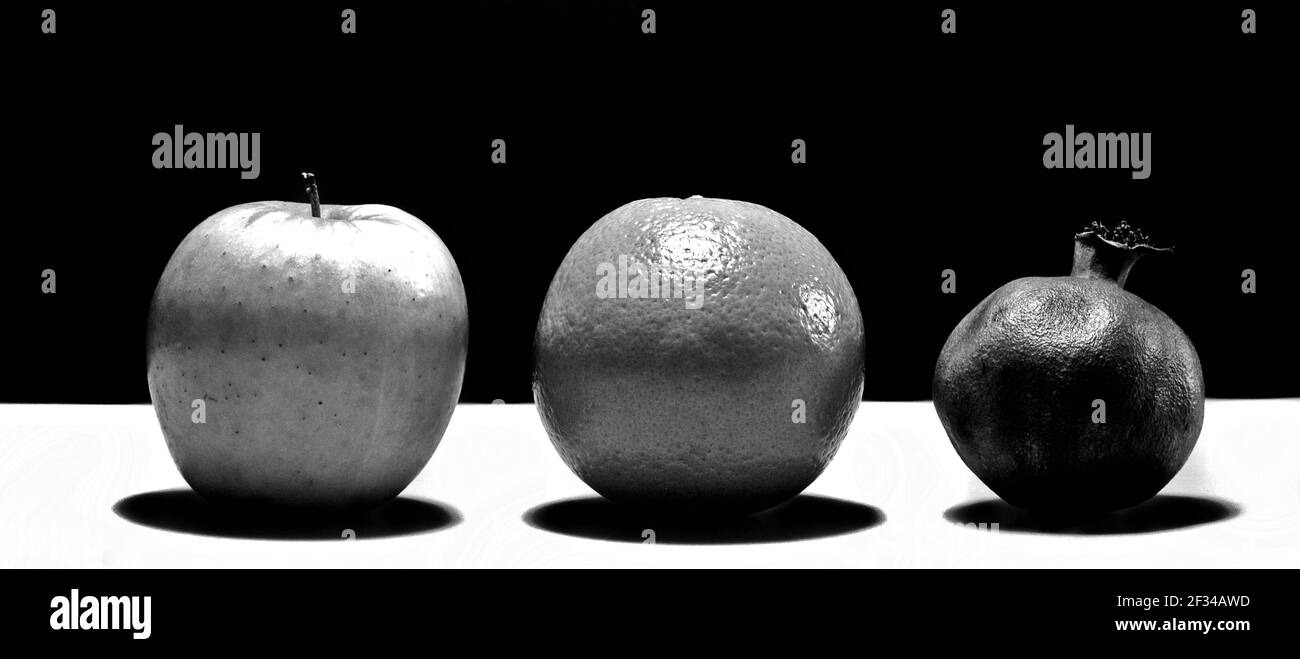 A grayscale photo of an apple, an orange, and a pomegranate on the table Stock Photo