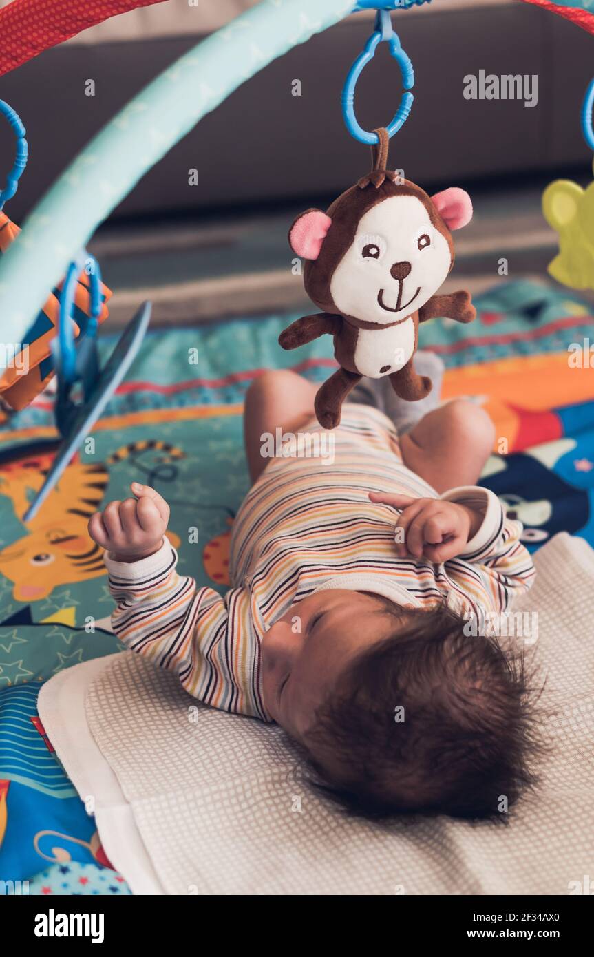 POZNAN, POLAND - Sep 12, 2017: Newborn baby boy sitting under a hanging plush monkey on a colorful mat Stock Photo