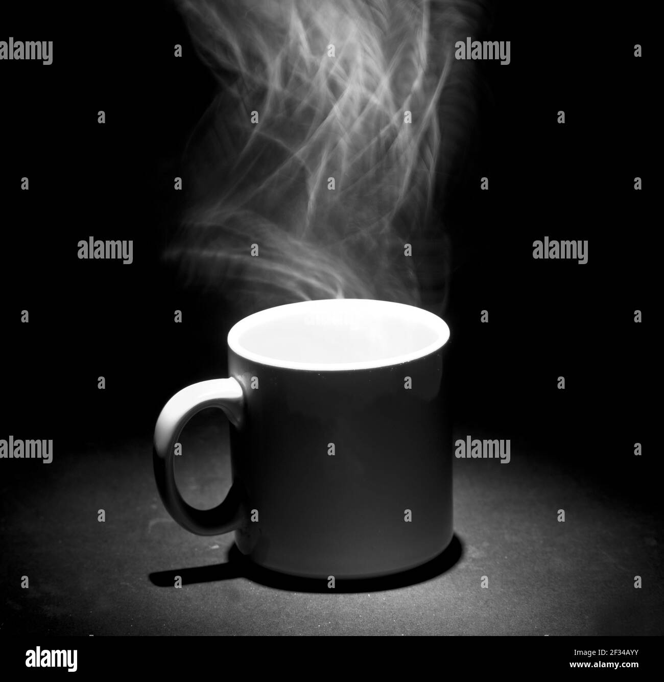 A grayscale photo of steam coming out of a mug on a black background Stock Photo