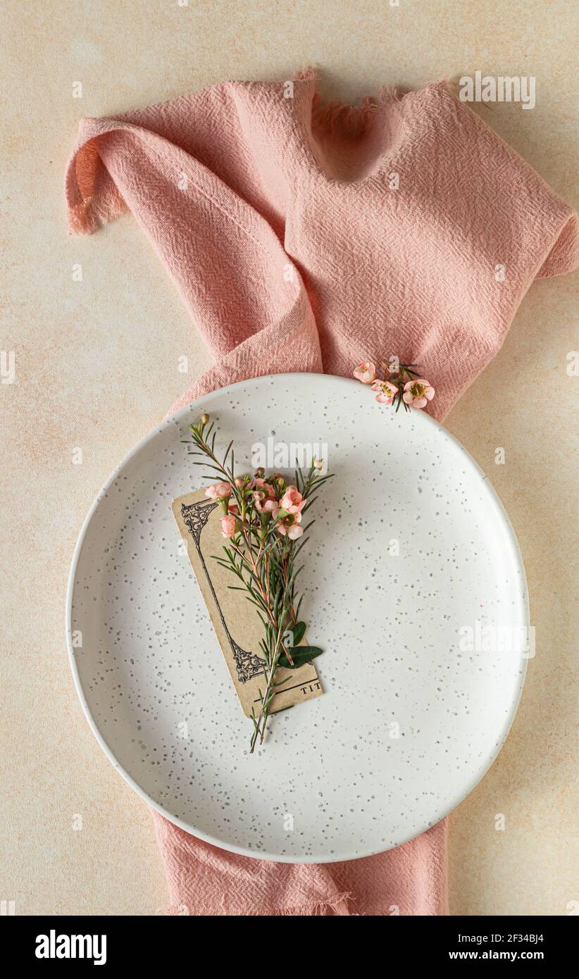 Romantic, wedding or spring table setting. Empty plate with card and little pink flowers, light concrete background. Selective focus. Stock Photo