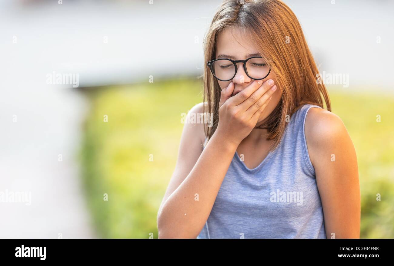 Teenager yawns outdoors holding hand in front of her mouth. Stock Photo