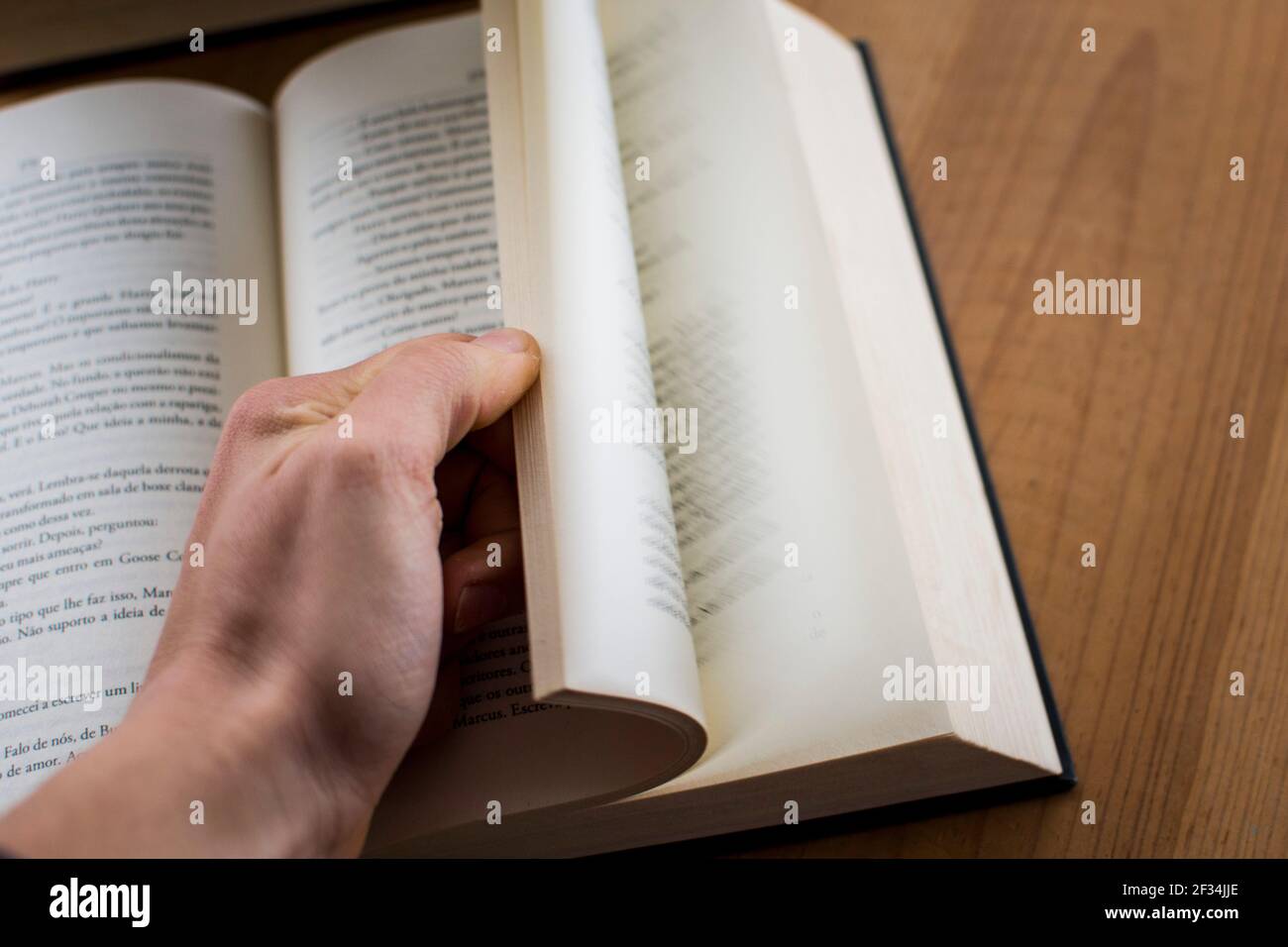 Human hand opening a hard cover book on top of a desk, sliding the pages Stock Photo
