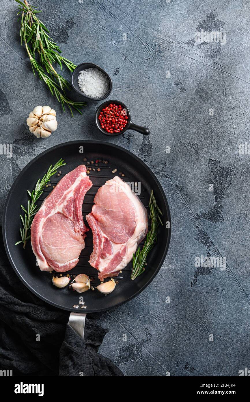 Pork steaks, fillets for grilling, baking in frying pan black skillet with herbs, spices top view flatlay space for text. Vertical Stock Photo
