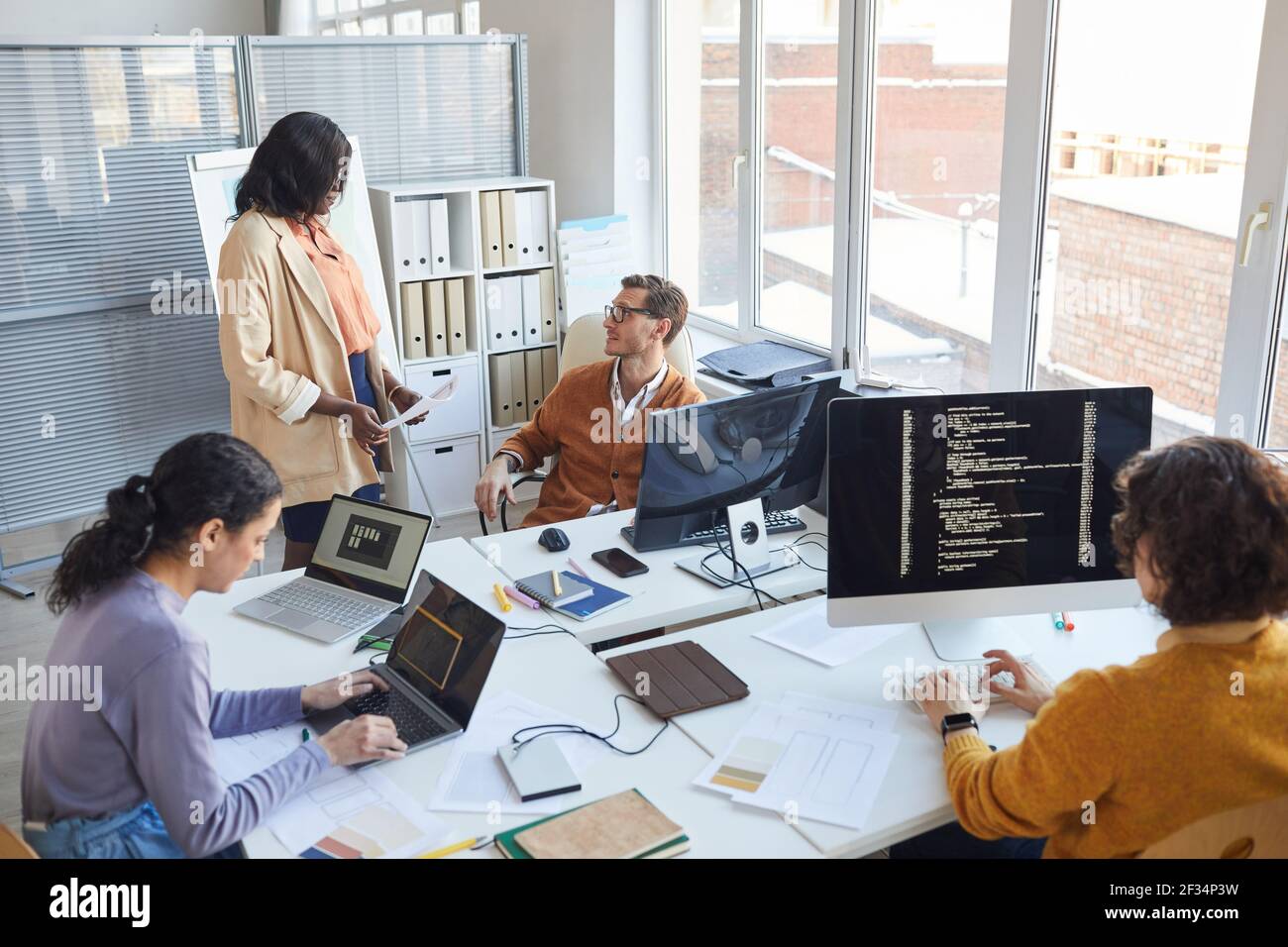 High angle view at multi-ethnic software development team using computers and writing code while collaborating on project in modern office, copy space Stock Photo