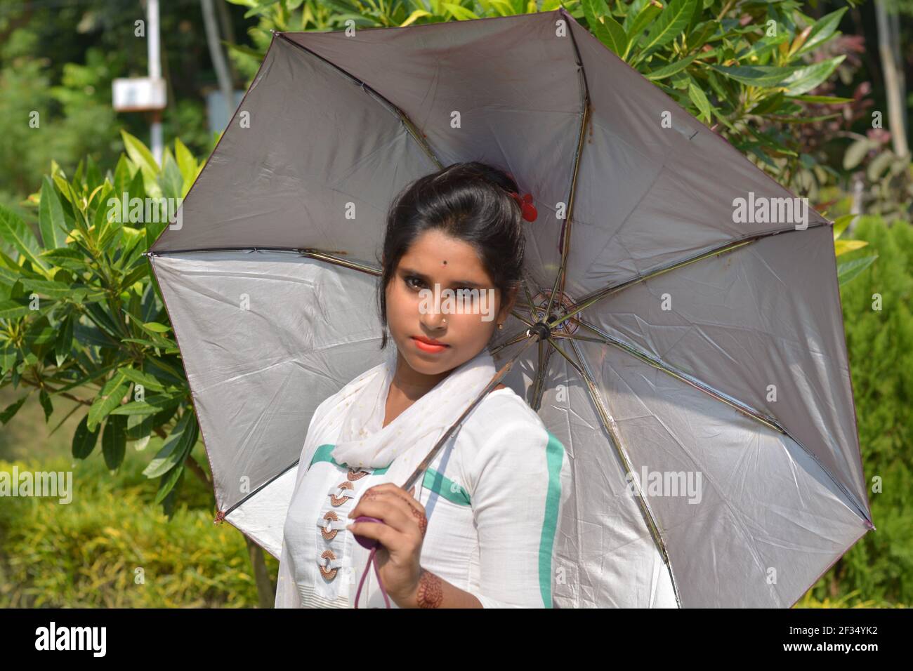 Teenage Indian Bengali girl wearing white cotton salwar holding an umbrella in a village farm, selective focusing Stock Photo