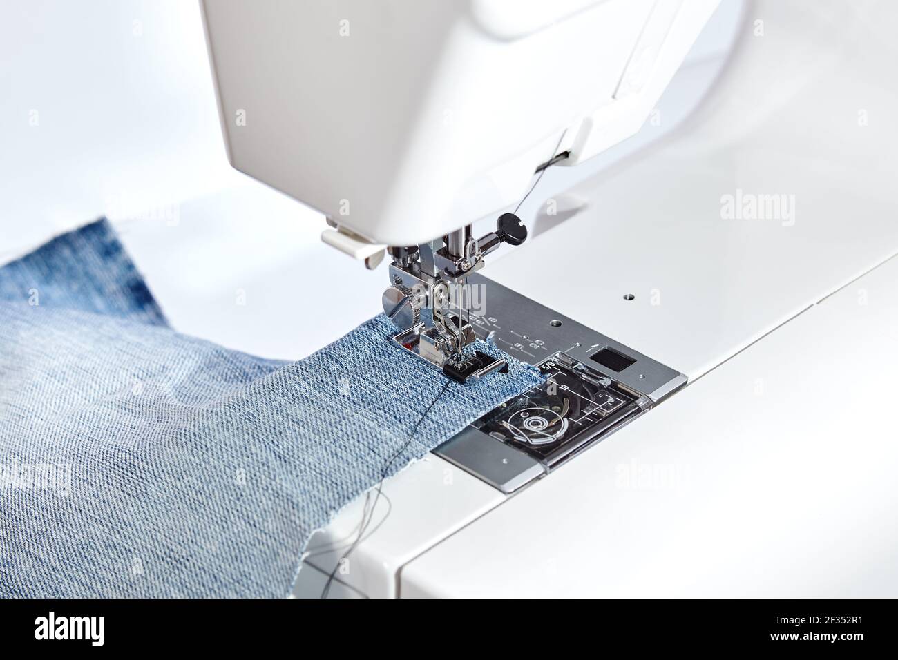 Sewing machine working part with blue denim cloth. A close-up shows a needle passing through tissue. Sewing machine with fabric and thread. Stock Photo