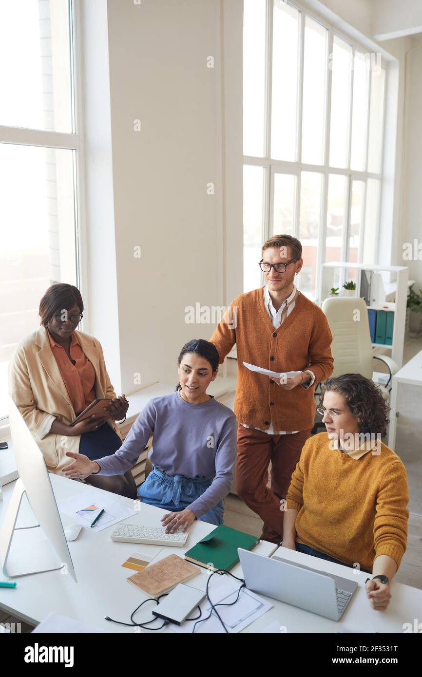 Vertical wide angle portrait of diverse IT development team discussing project while working on software production in office, copy space Stock Photo