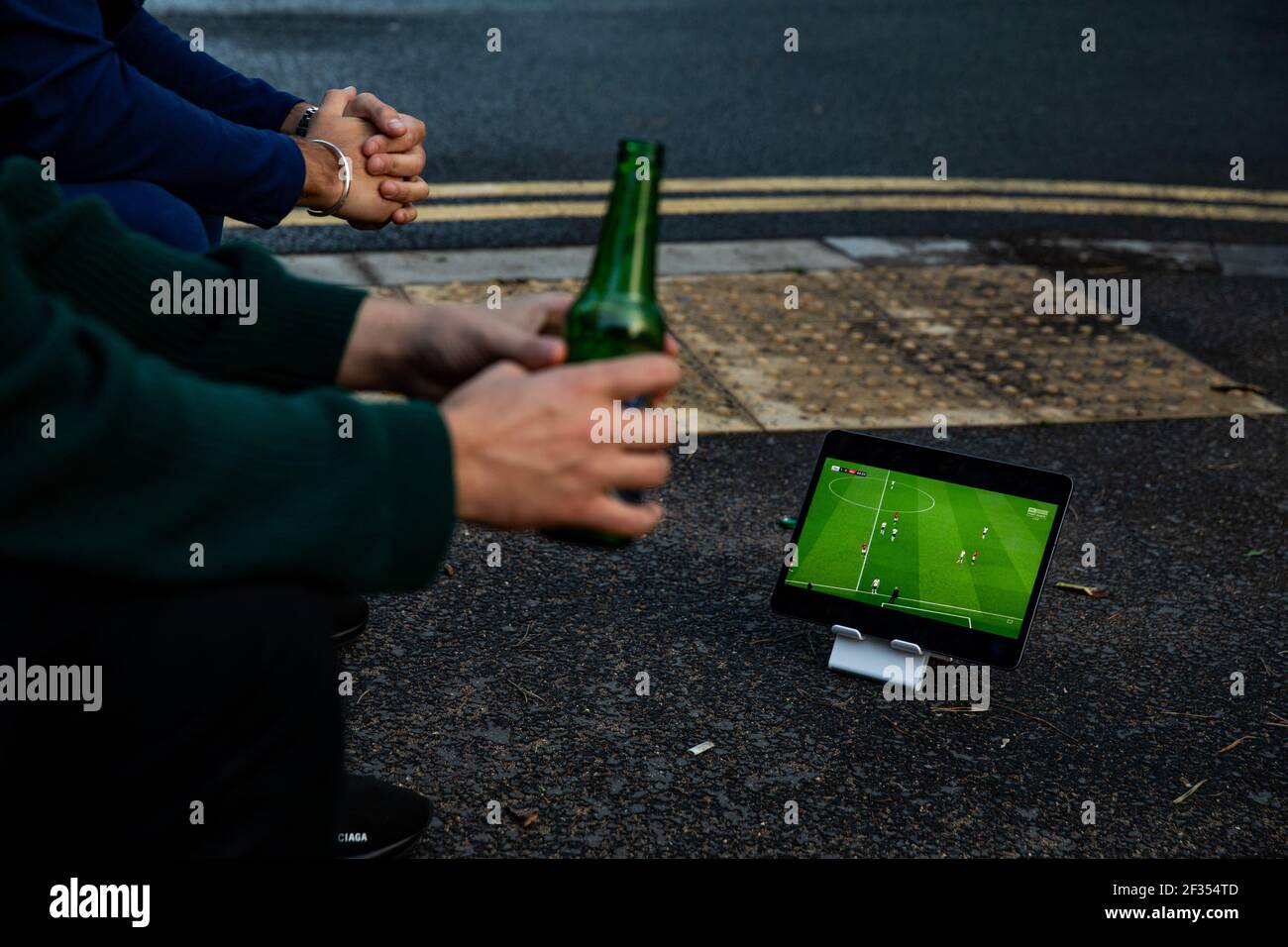 Two Tottenham Hotspur fans watching the game Sky GO app on the iPad outside the ground during the Premier League match back following the Coronavirus Stock Photo