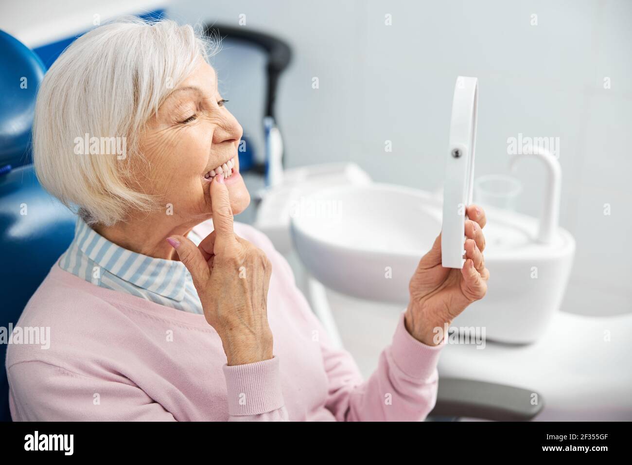 Elderly person with mirror pushing her tooth with finger Stock Photo