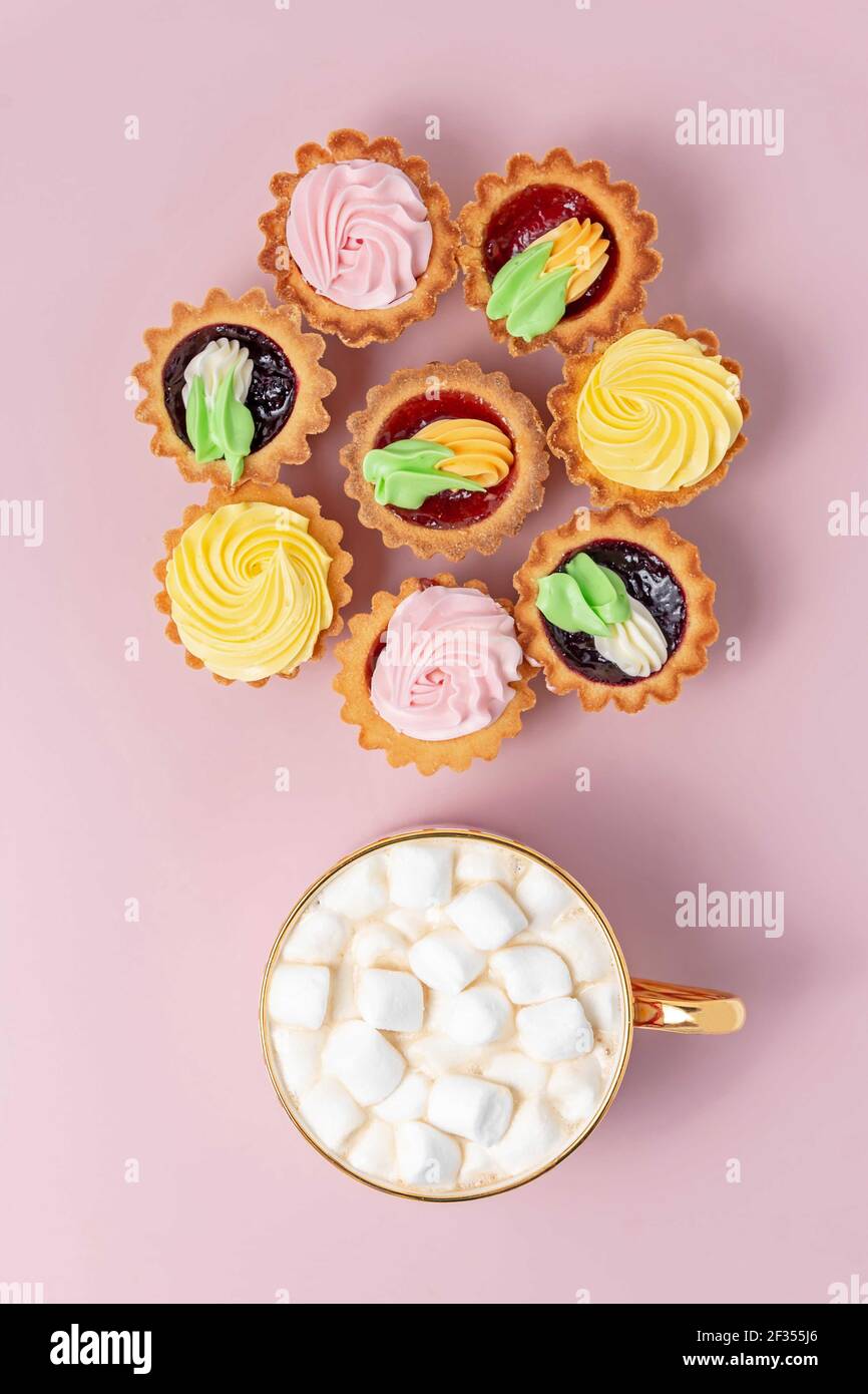 Tasty cupcakes and cup of cocoa with marshmallows on pastel pink background. Stock Photo