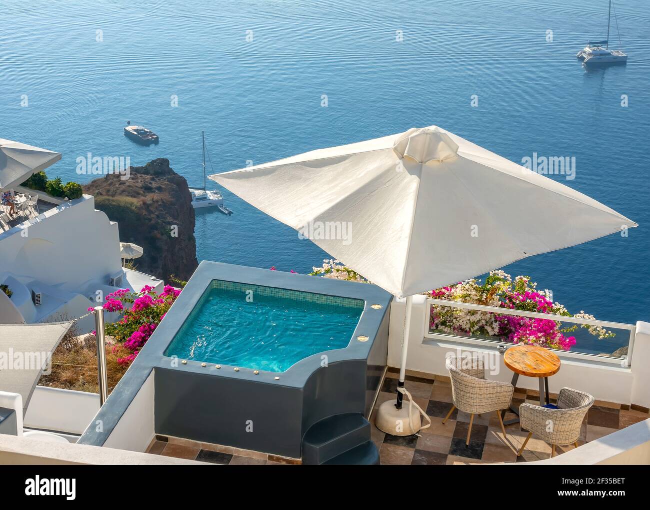 Santorini. Terraces on the high shore of Thera Island. Swimming pool and loungers for relaxing in sunny weather. Yachts by the shore Stock Photo
