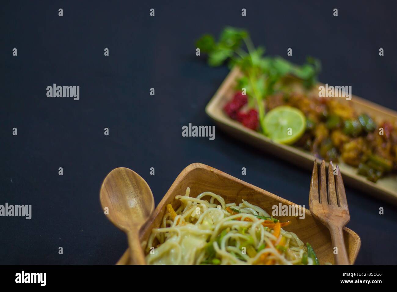 chilli chicken and noodles served on wooden plates with spoon and fork. delicious chinese food for copy space background. shallow depth of field.adver Stock Photo