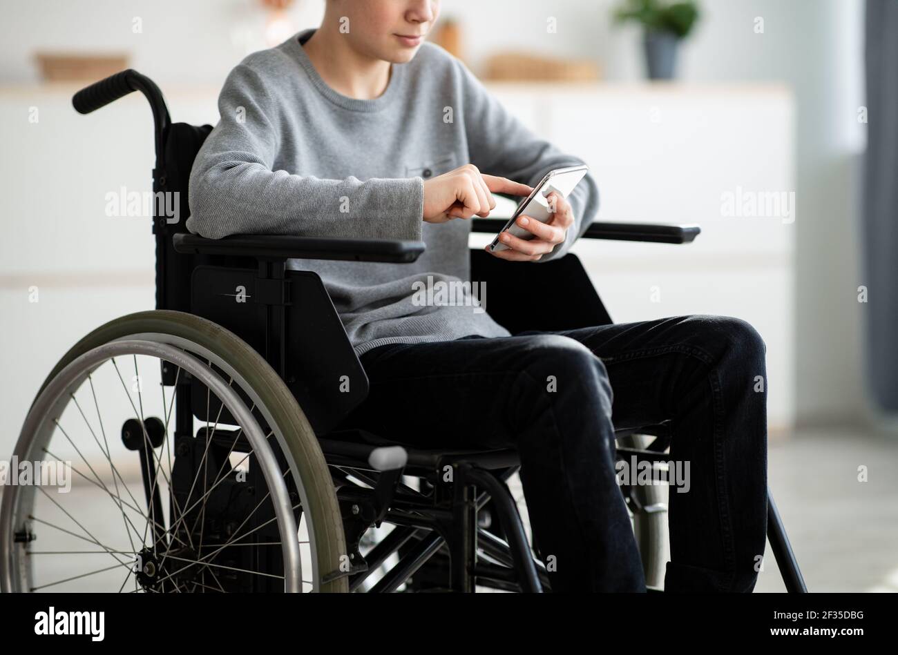 Cropped view of disabled teen boy in wheelchair using smartphone at home, closeup Stock Photo
