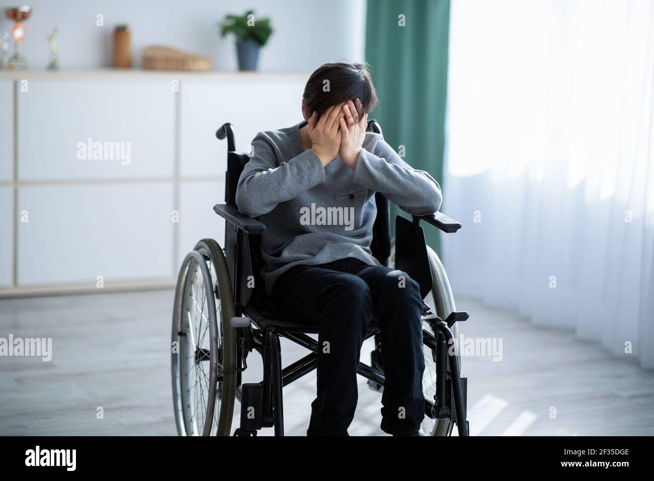 Depression in teens with disability. Unhappy adolescent in wheelchair crying from loneliness at home Stock Photo