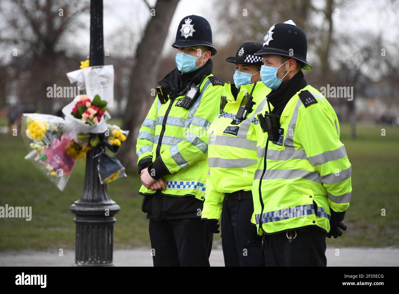 Police officers stand next to floral tributes left at the band stand in Clapham Common, London, for murdered Sarah Everard. Serving police constable Wayne Couzens, 48, appeared in court on Saturday charged with kidnapping and murdering the 33-year-old marketing executive, who went missing while walking home from a friend's flat in south London on March 3. Picture date: Monday March 15, 2021. Stock Photo