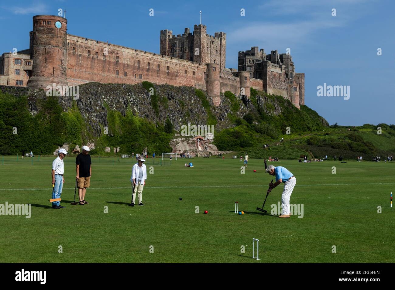 Member of the Bamburgh Croquet Club playing with Bamburgh castle in the background in Northumberland Stock Photo