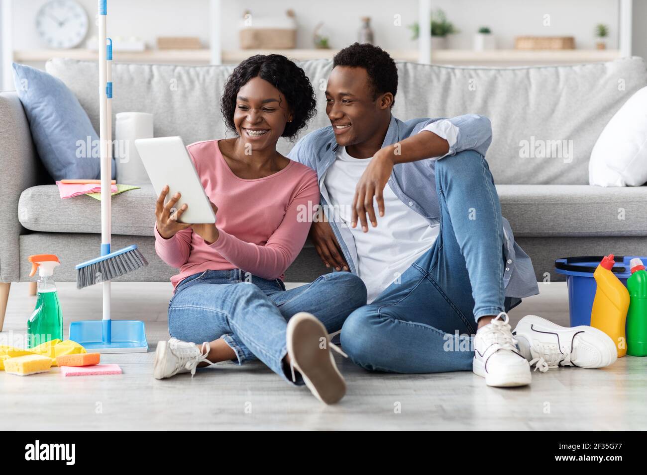 Black couple with cleaning tools resting, using digital tablet Stock Photo