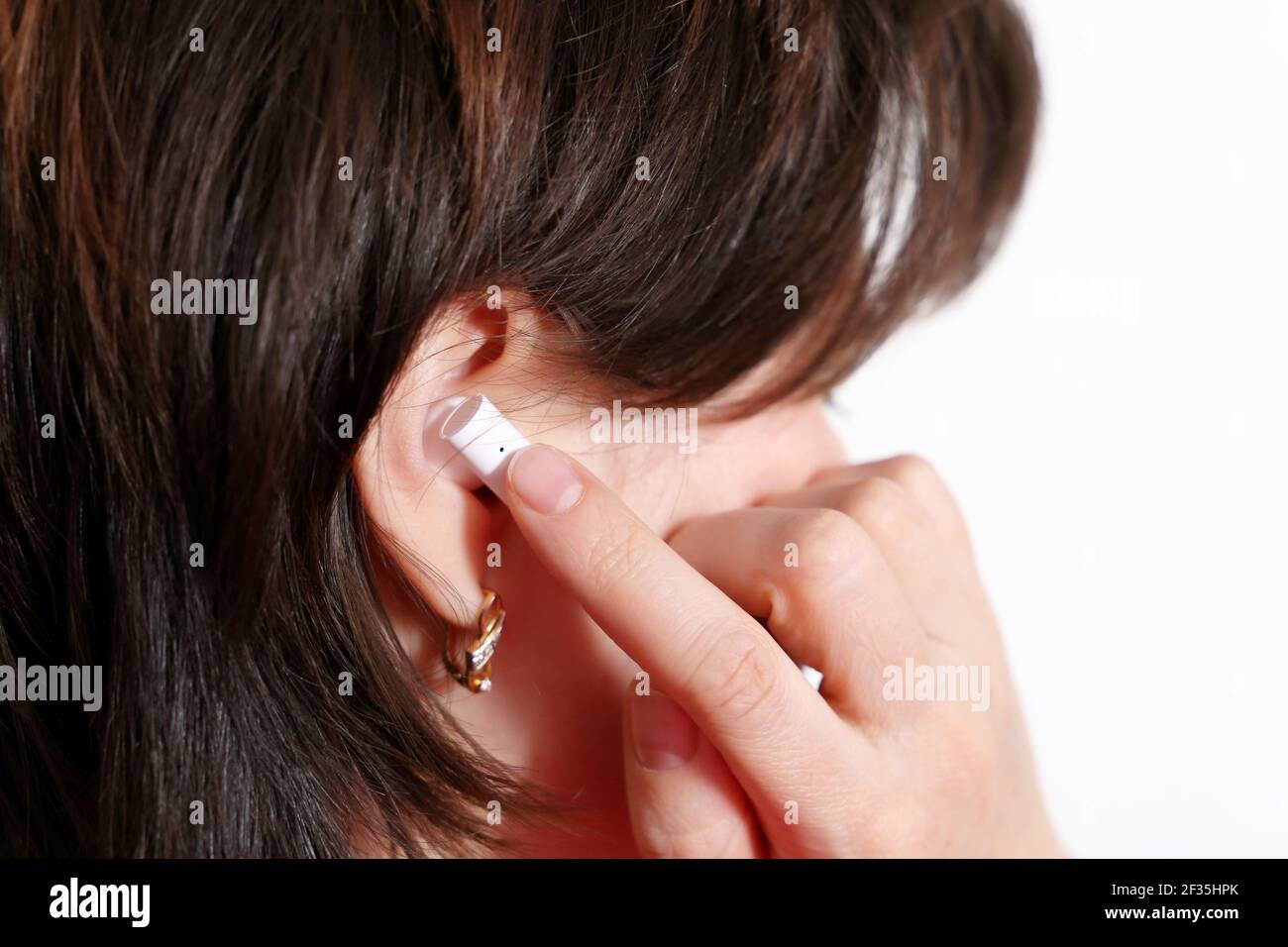Woman touching wireless earphone in the ear. Headset, listening to music and voice call concept Stock Photo