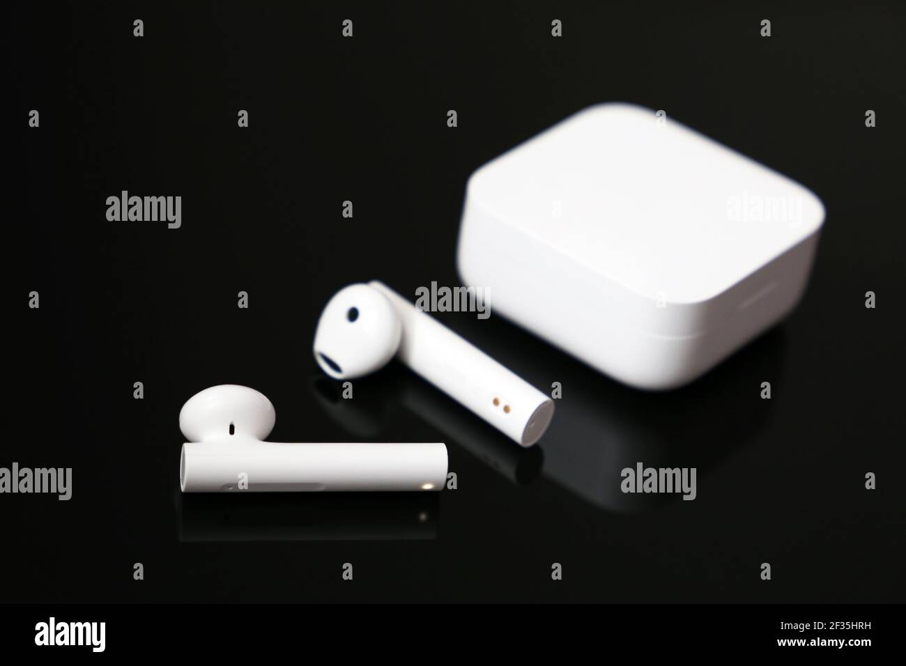 Wireless earphones with white charging case on black glass table. Headset for listening to music and voice call Stock Photo