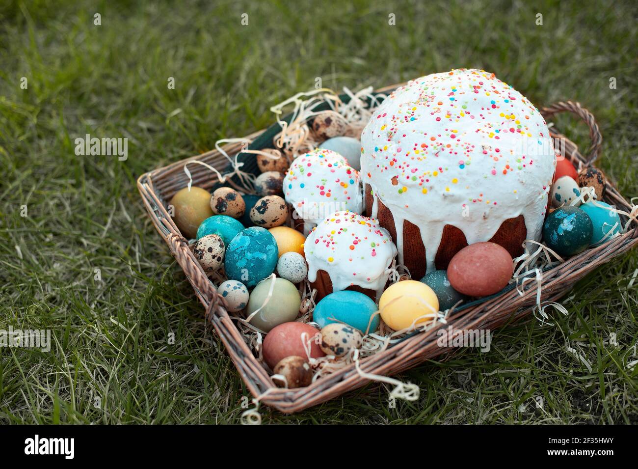 Wicker basket with Easter cake and eggs on green grass background Stock Photo