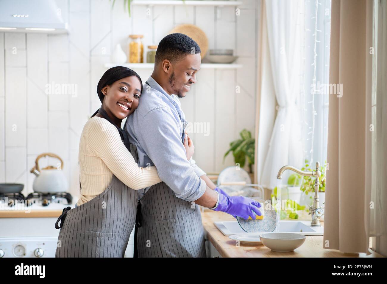 Cheerful black couple washing dishes together at kitchen, free space