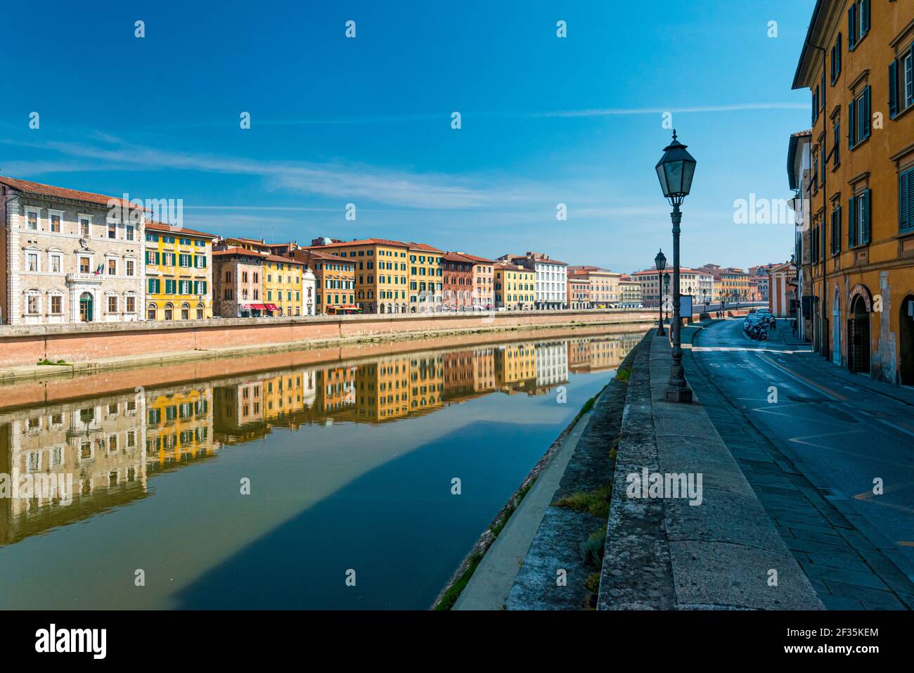 Various color houses at riverbank reflecting on water surface of Arno river, Pisa, Italy. Empty streets in touristic destination. Stock Photo