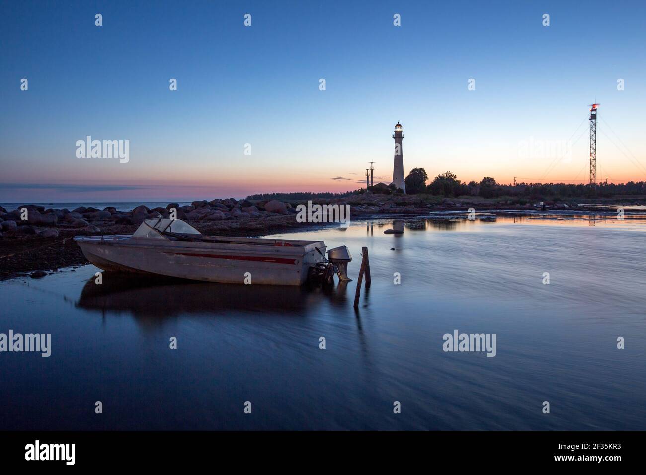 Moon lit seascape view with the fishing boat in front and historic  lighthouse and maritime radar tower in background during the light Nordic  midsummer Stock Photo - Alamy