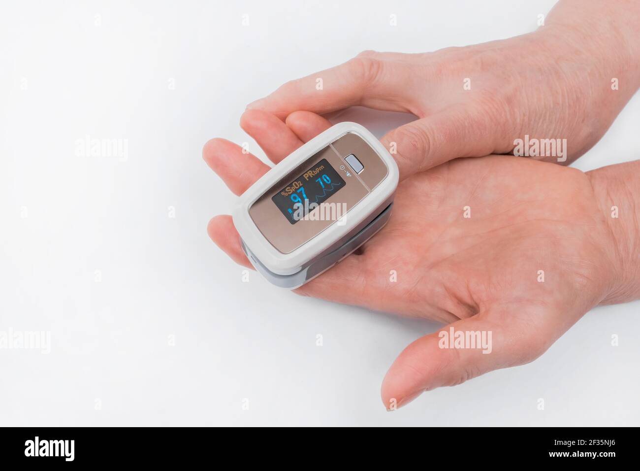 The hands of an elderly woman hold a modern device to measure the saturation of the pulse oximeter on a white background. Stock Photo