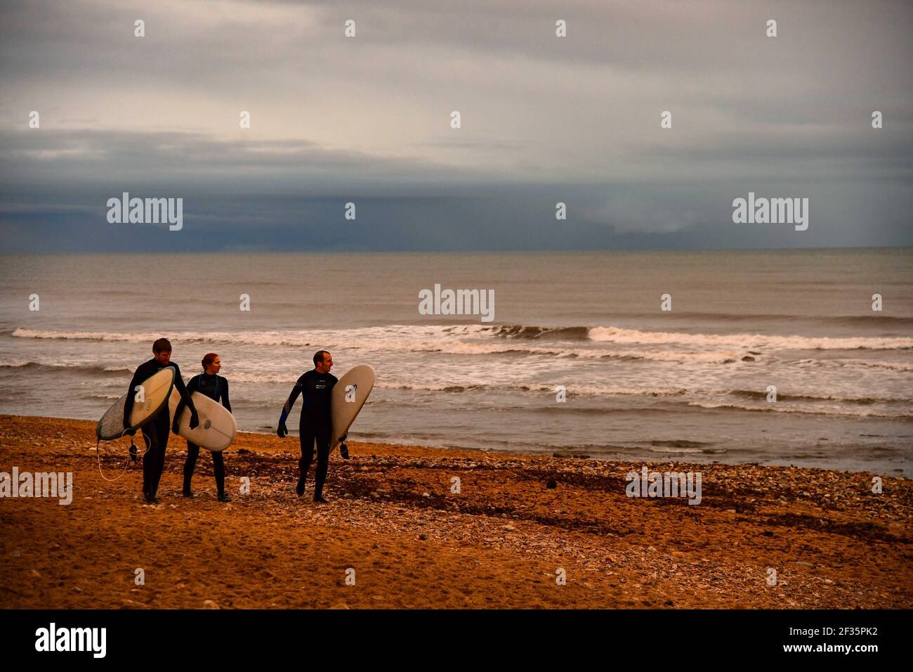 3 surfers walk home along a beach in Cornwall after surfing in the sea Stock Photo