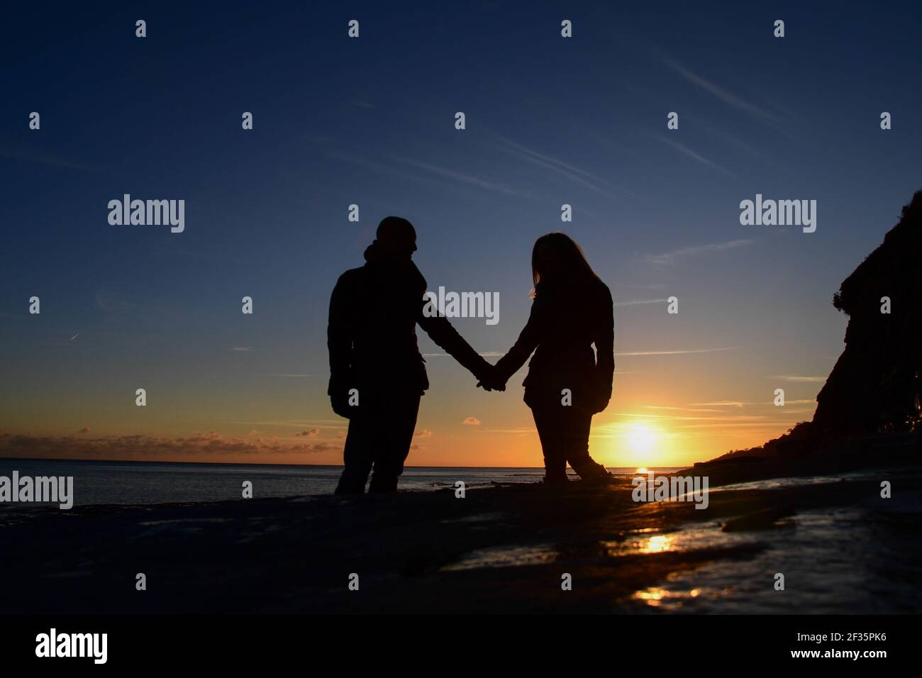Two people holding hands on a beach at sunset Stock Photo