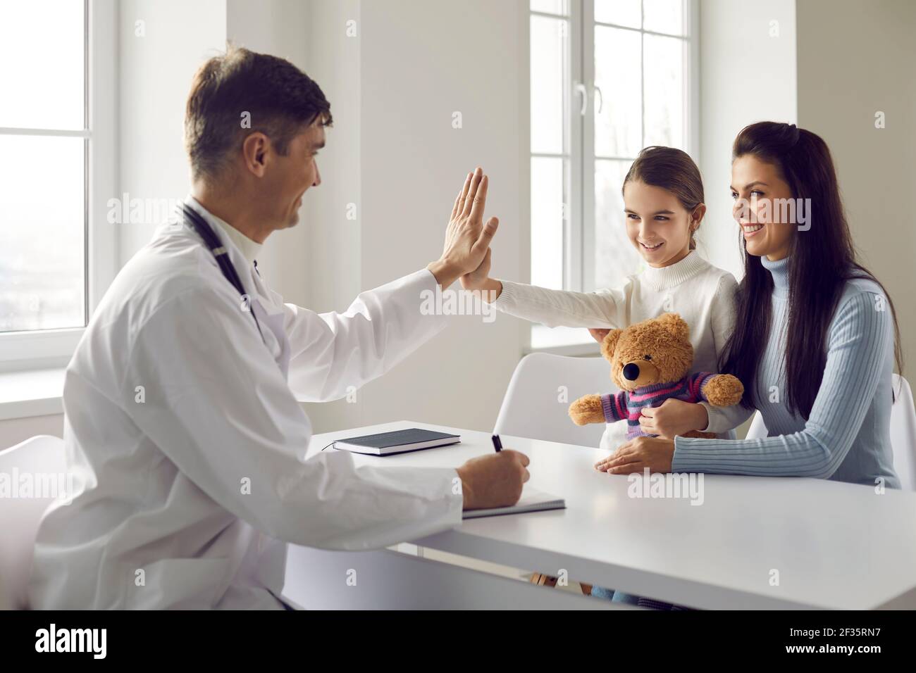 Friendly pediatrician gives five to his little girl patient in the doctor's office. Stock Photo