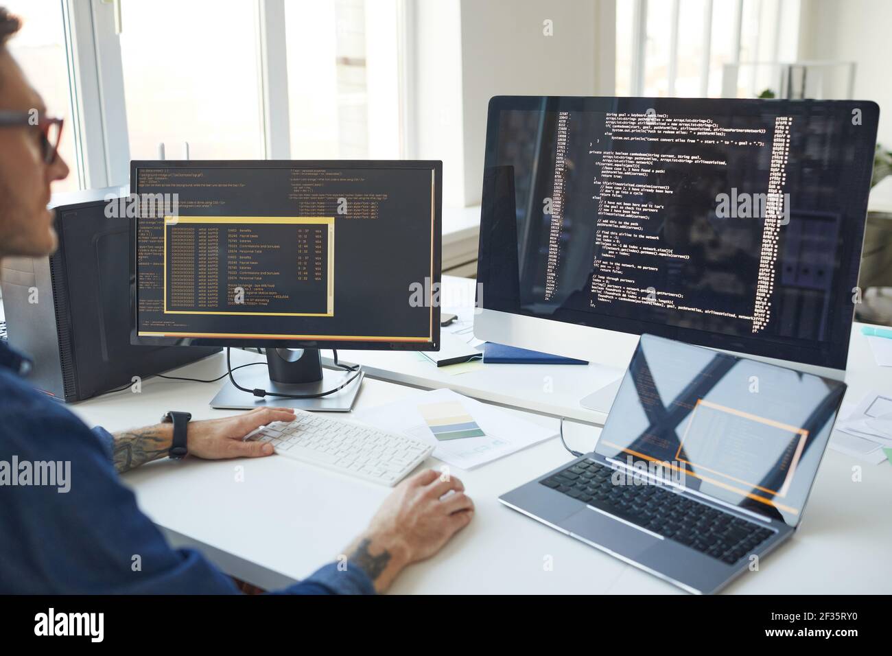 Side view at male programmer writing code while using multiple computers in IT developers office , copy space Stock Photo