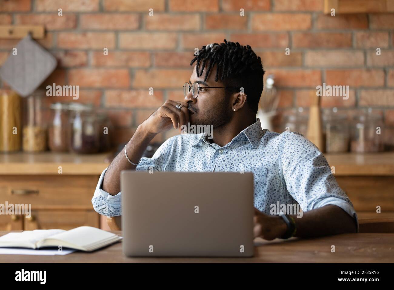 African man sit by laptop look aside ponder on problem Stock Photo