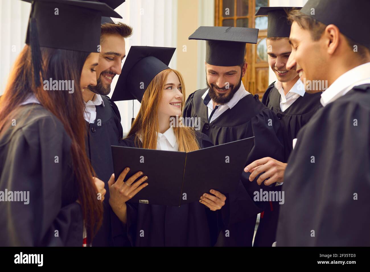 Group of young smiling happy students university graduates standing looking at girl mate diploma Stock Photo