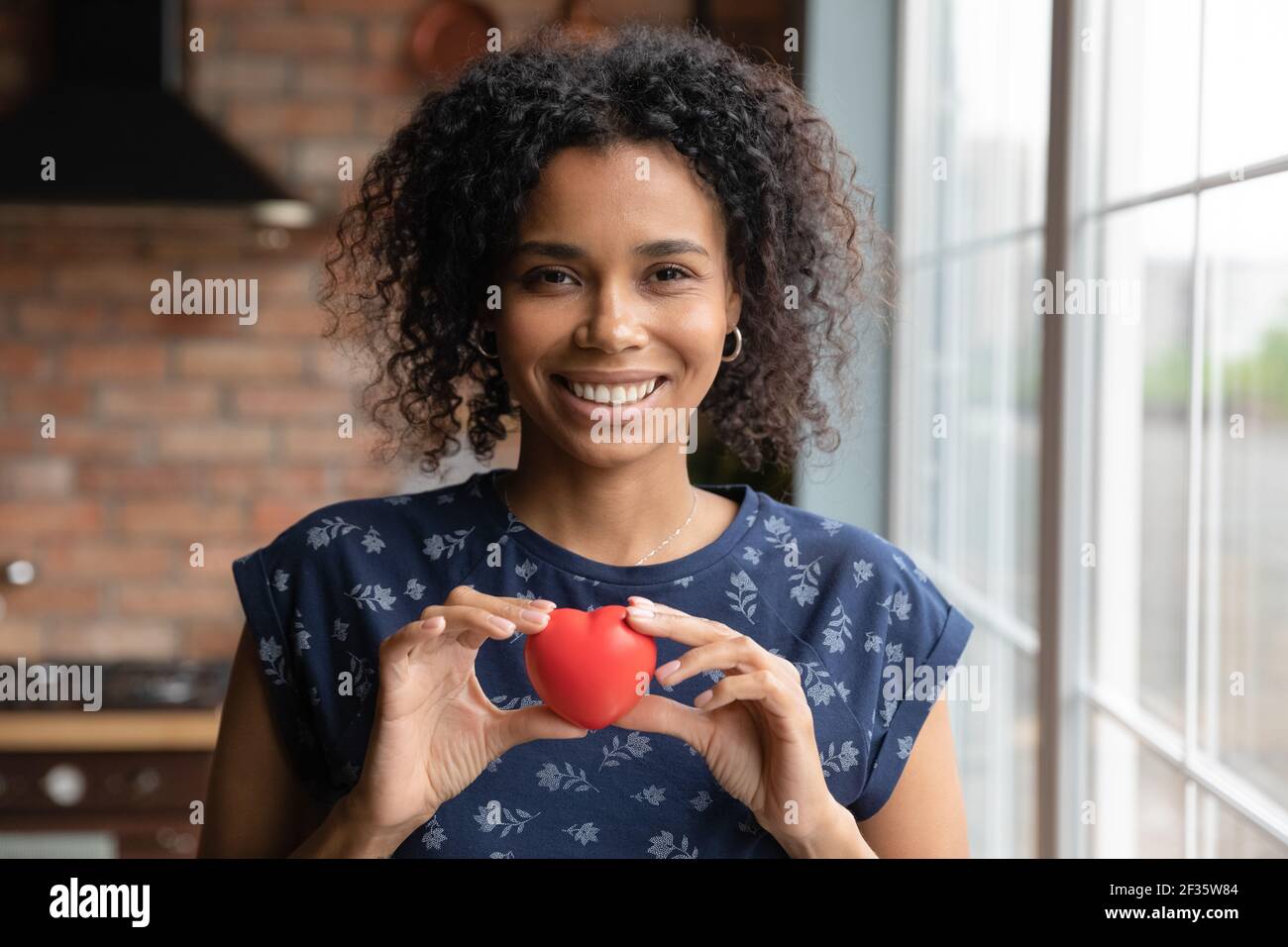 Happy black woman looking at camera holding red toy heart Stock Photo