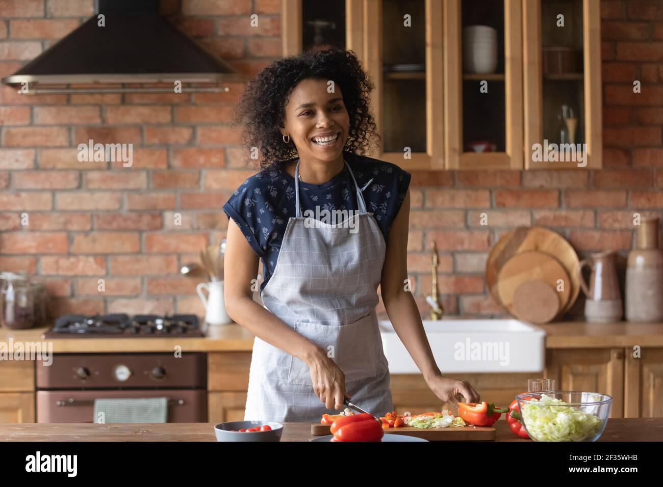 Joyful young afro american lady cut vegetable salad for lunch Stock Photo