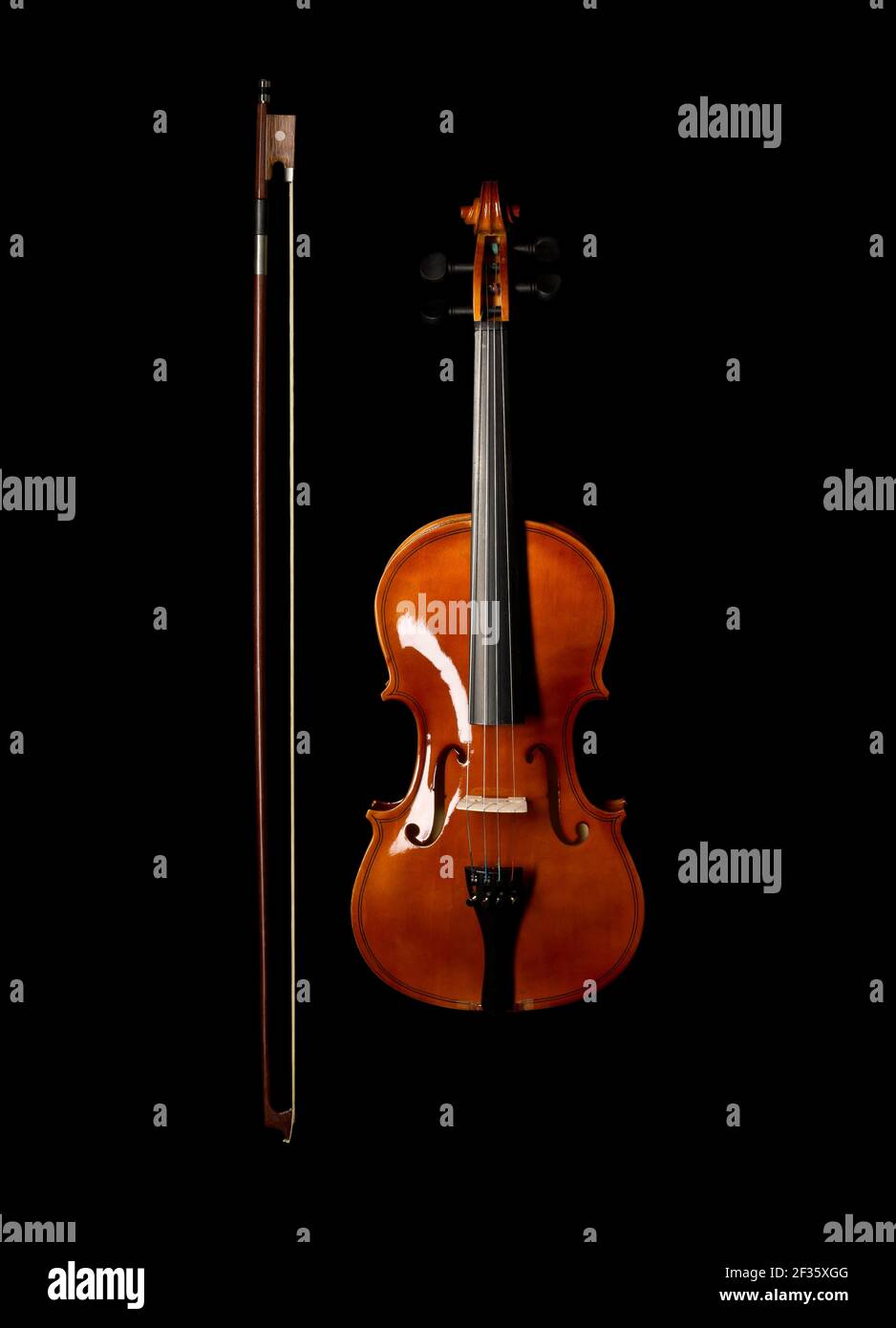Brown wooden fiddle or violin, classic musical instrument, with bow next to it isolated over black background, flat lay top view from above Stock Photo