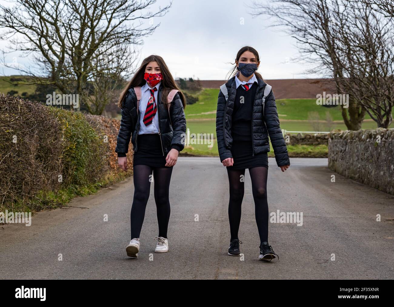 East Lothian, Scotland, United Kingdom, 15th March 2021. School children return to secondary school: Twins, Louisa and Imogen, aged 12 years and in S1 returned to North Berwick High School today for the first time since the recent lockdown during the coronavirus pandemic, but only for 3 hours today for the whole week as they get off the school bus at Kilduff Stock Photo