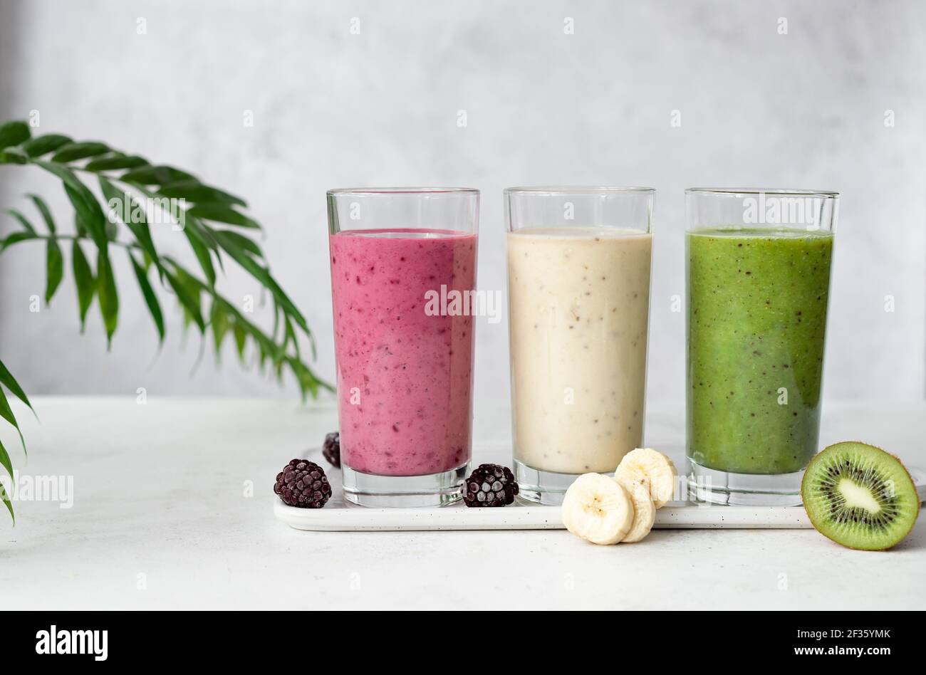 different types of smoothies on a gray background with green leaves