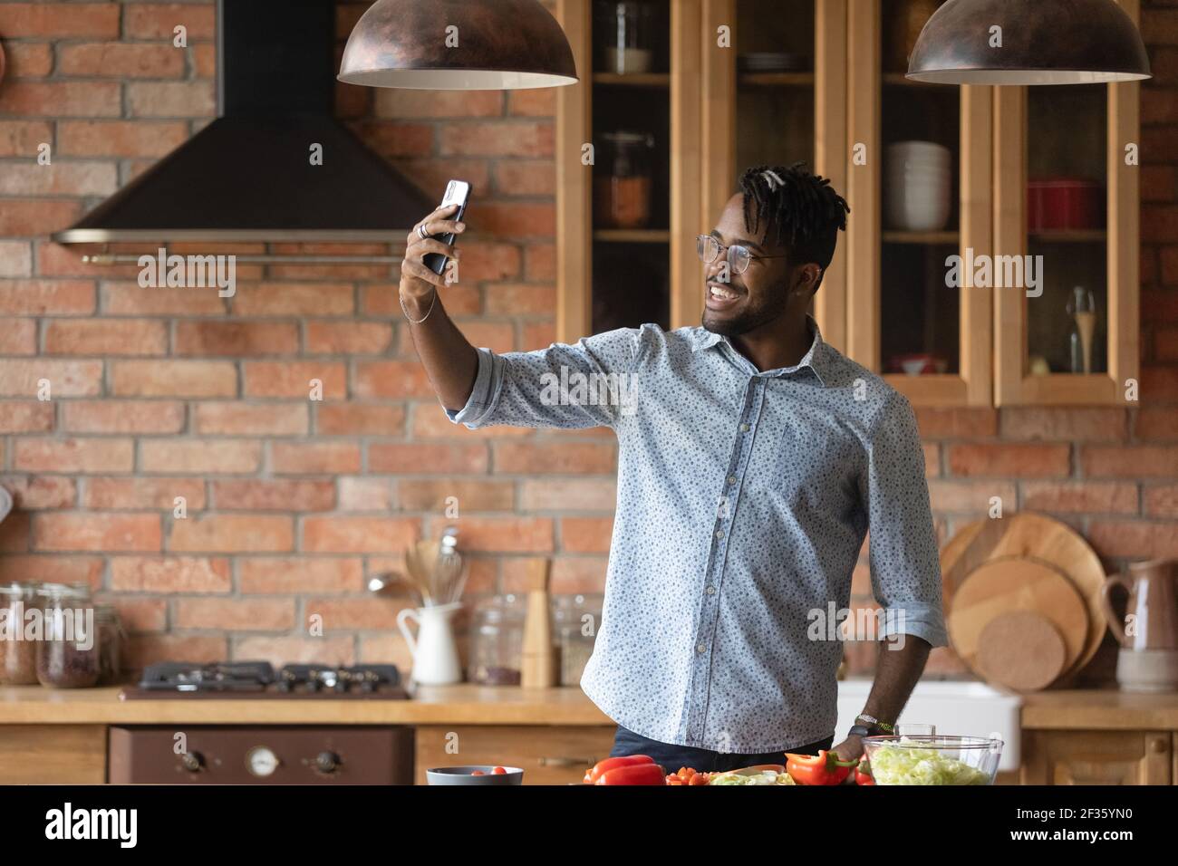 Joyful young black male cooking food and posing for selfie Stock Photo