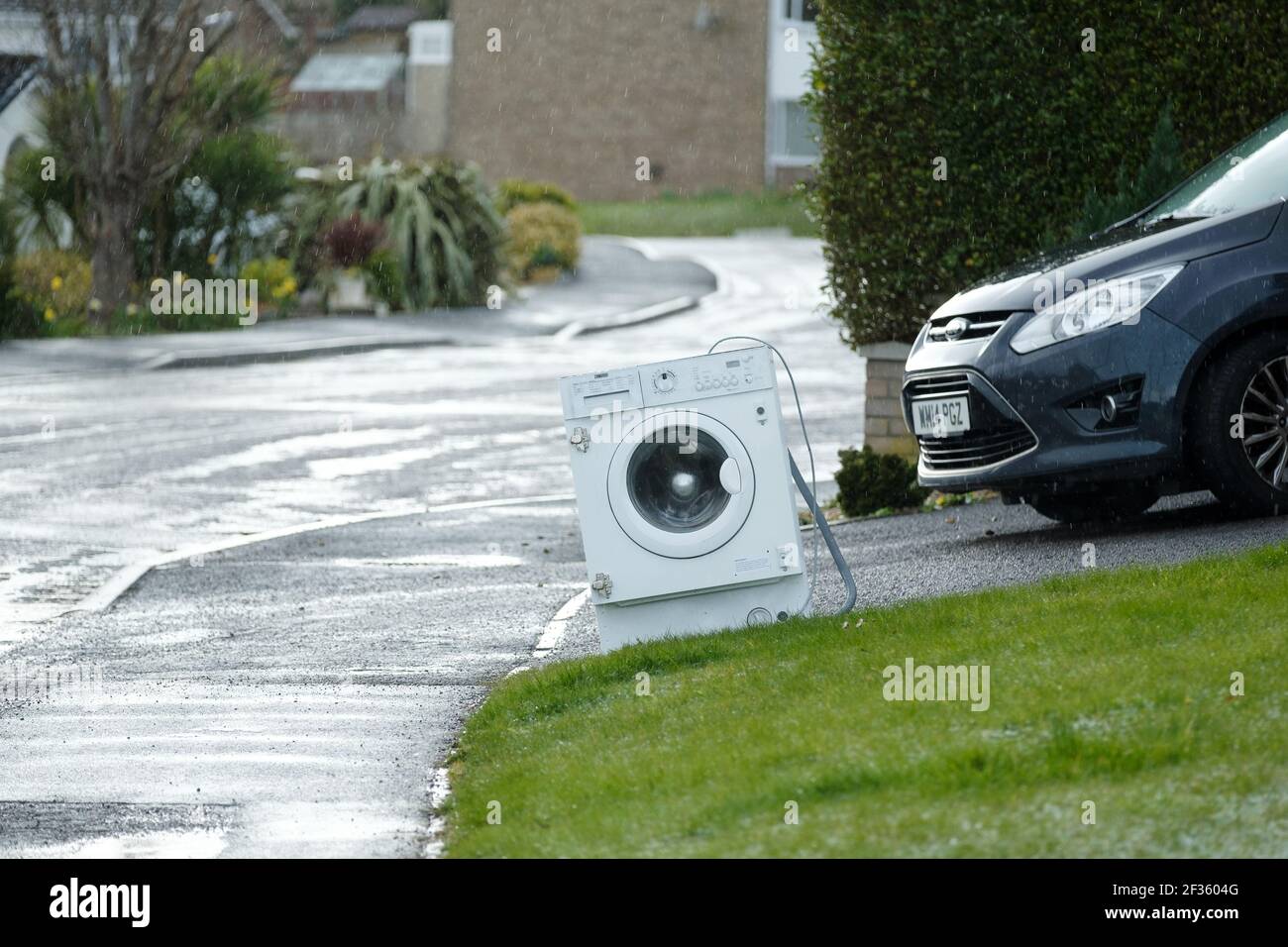 An old washing machine is left at the end of a house drive or driveway. It’s for collection by the local council or local waste metal collector Stock Photo