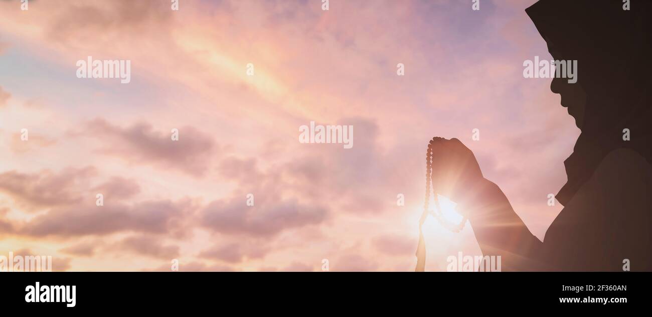 Silhouette Young muslim woman hijab honesty pray to God on sunset panoramic mosque background concept for eid mubarak, life and spiritual of islam gir Stock Photo