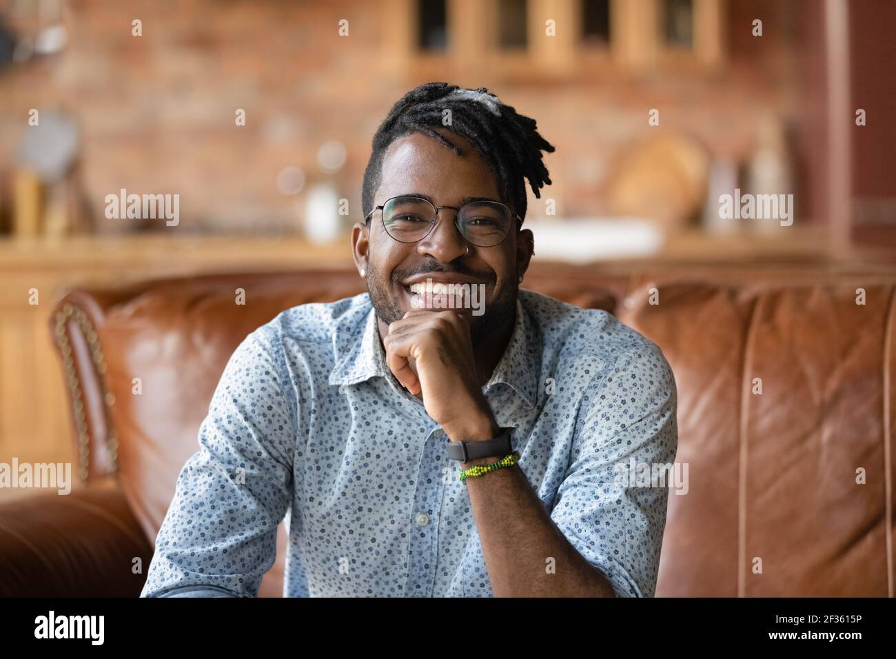Smiling young black male sitting on sofa looking at camera Stock Photo