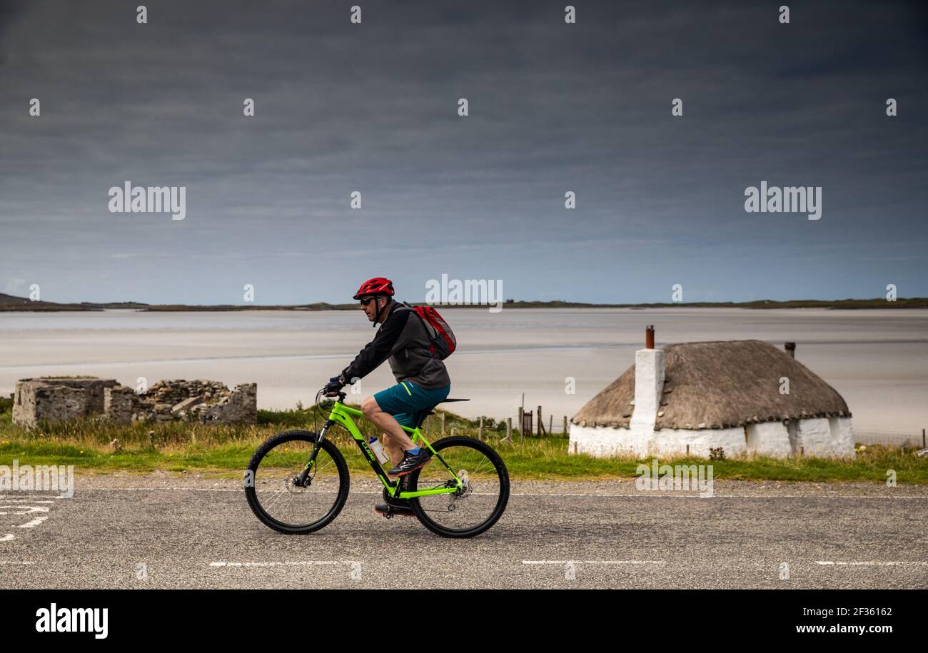 A cyclists riding past a thatched house in Malacleit in North Uist in the Outer Hebrides, Scotland Stock Photo
