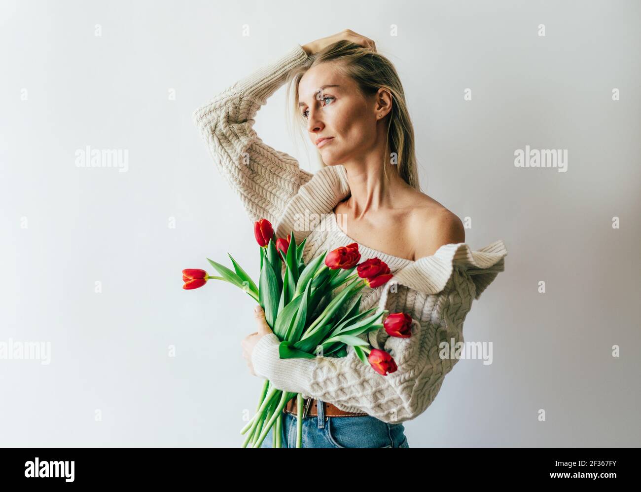 Young pretty confident emancipated woman with a bouquet of tulips against a white wall background. Stock Photo