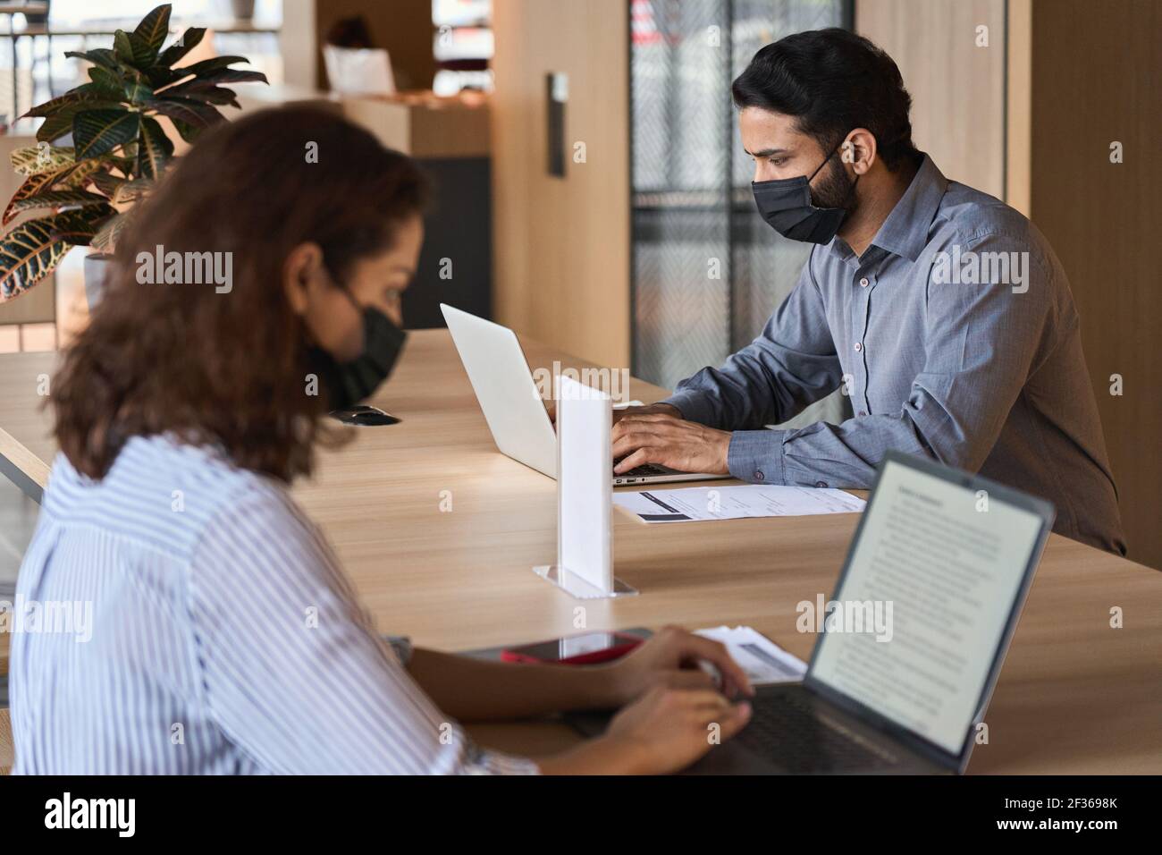 Diverse people wearing face masks working on laptops keeping safe distance. Stock Photo