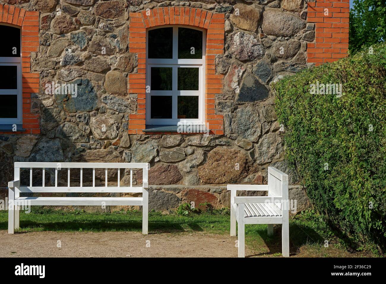 Two white benches standing in the courtyard of an old stone house on a bright sunny day Stock Photo